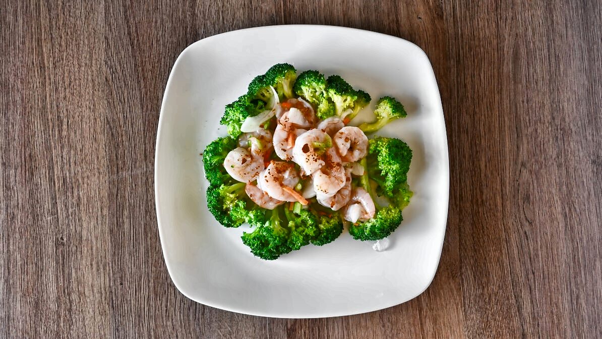 Garlic shrimp with broccoli from above: pink shrimp over bright green broccoli florets with small pieces of onion and carrot, on a white square plate.