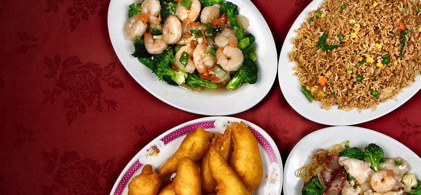Four dishes shot from above on crimson damask: shrimp with broccoli, vegetable fried rice, deep-fried shrimp on a pink-bordered plate, and chow mein.