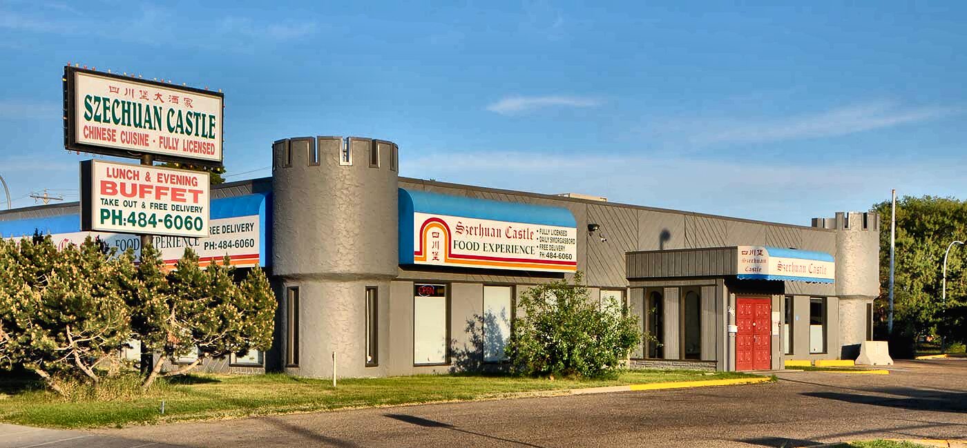 The Szechuan Castle building in daylight: a long grey stucco frontage with two crenellated stone turrets flanking the entrance, blue-and-white awnings, red panelled doors, and roadside signs reading SZECHUAN CASTLE — CHINESE CUISINE — FULLY LICENSED and LUNCH & EVENING BUFFET.