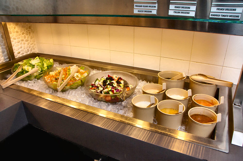 The salad bar bedded on crushed ice: bowls of chopped romaine, carrot-and-cabbage slaw and a bean-and-olive salad, with tubs of dressing and ladles beside them.