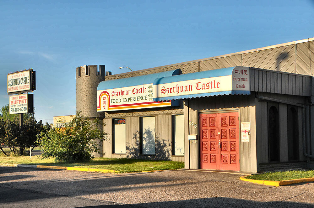 The entrance in low golden light: a blue-and-white Szechuan Castle awning over red panelled double doors, the street number 15415 on the wall, and a crenellated turret to the left.